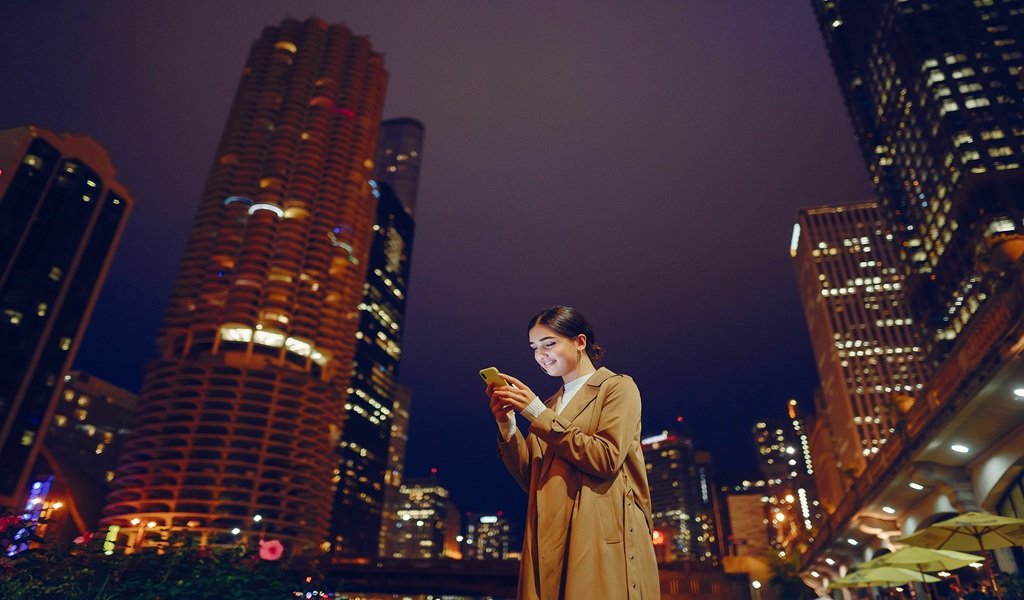 young brunette girl standing at night with phone by Chicago skyline