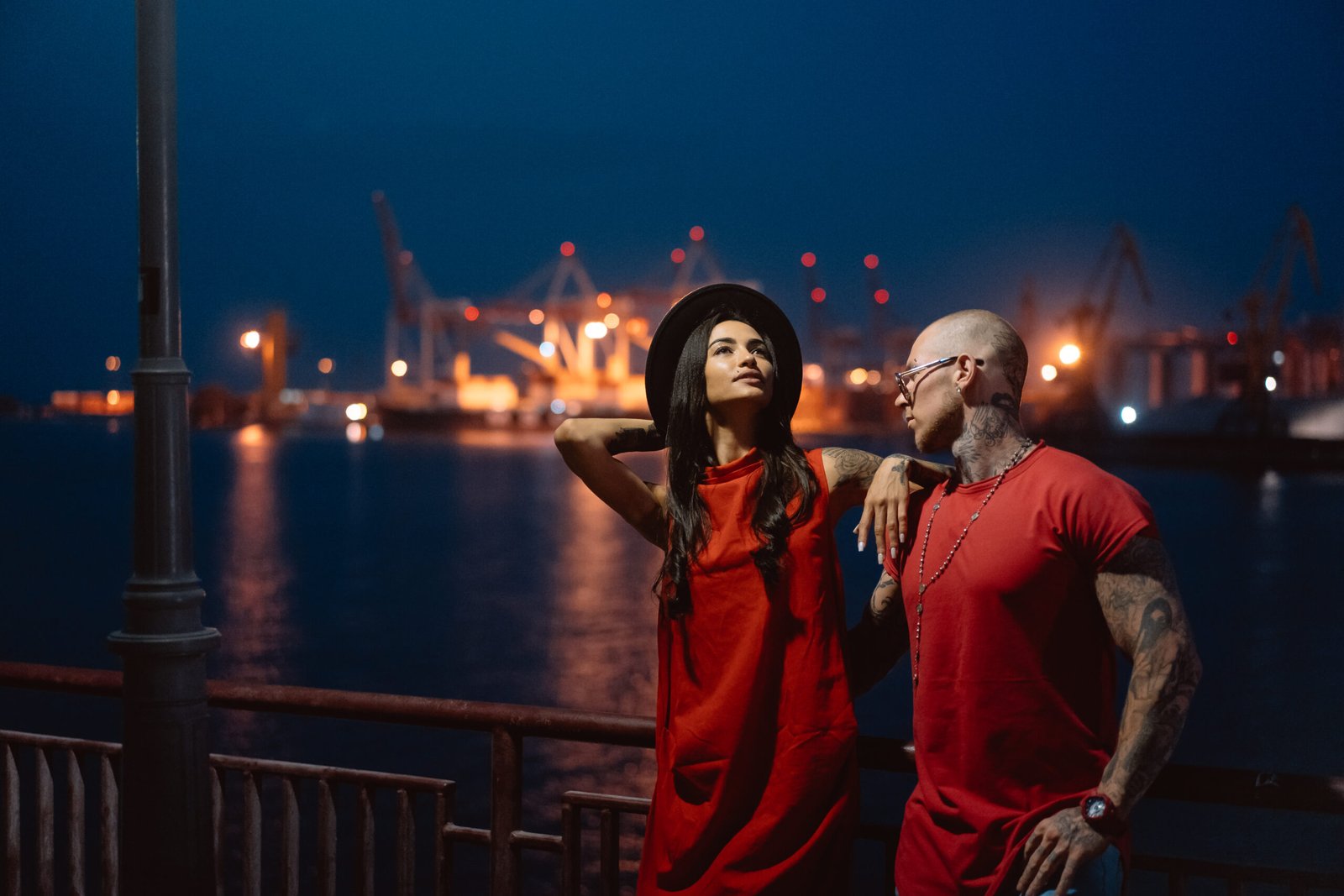 The young, modern, couple of lovers pose for a camera on the night promenade. The port is in the background